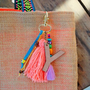 May include: A pink and purple tassel keychain with a wooden letter Y charm. The keychain is attached to a gold metal ring and has colorful beads and a blue ribbon.