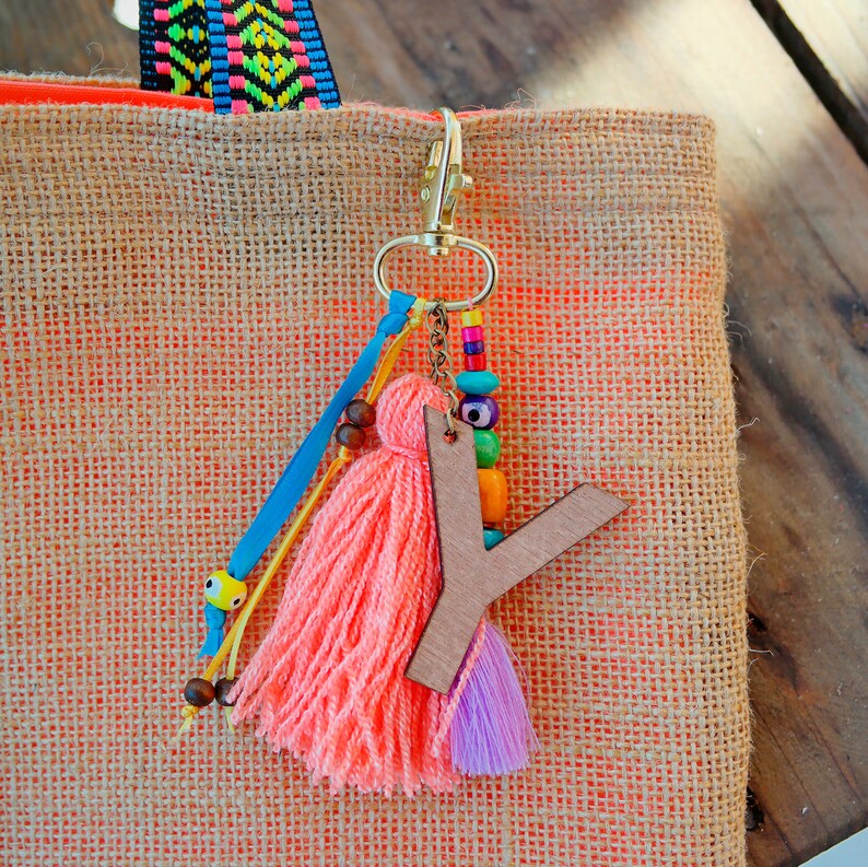 May include: A pink and purple tassel keychain with a wooden letter Y charm. The keychain is attached to a gold metal ring and has colorful beads and a blue ribbon.