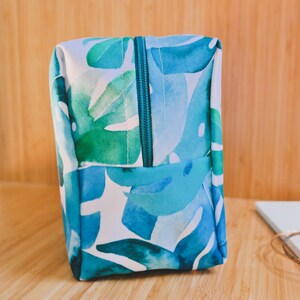 May include: A blue and green toiletry bag with a zipper closure. The bag has a watercolor-style print of tropical leaves.