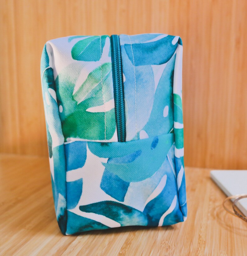 May include: A blue and green toiletry bag with a zipper closure. The bag has a watercolor-style print of tropical leaves.