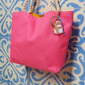 May include: A bright pink tote bag with a yellow lining and a wooden charm with the letter "F" hanging from the handle.