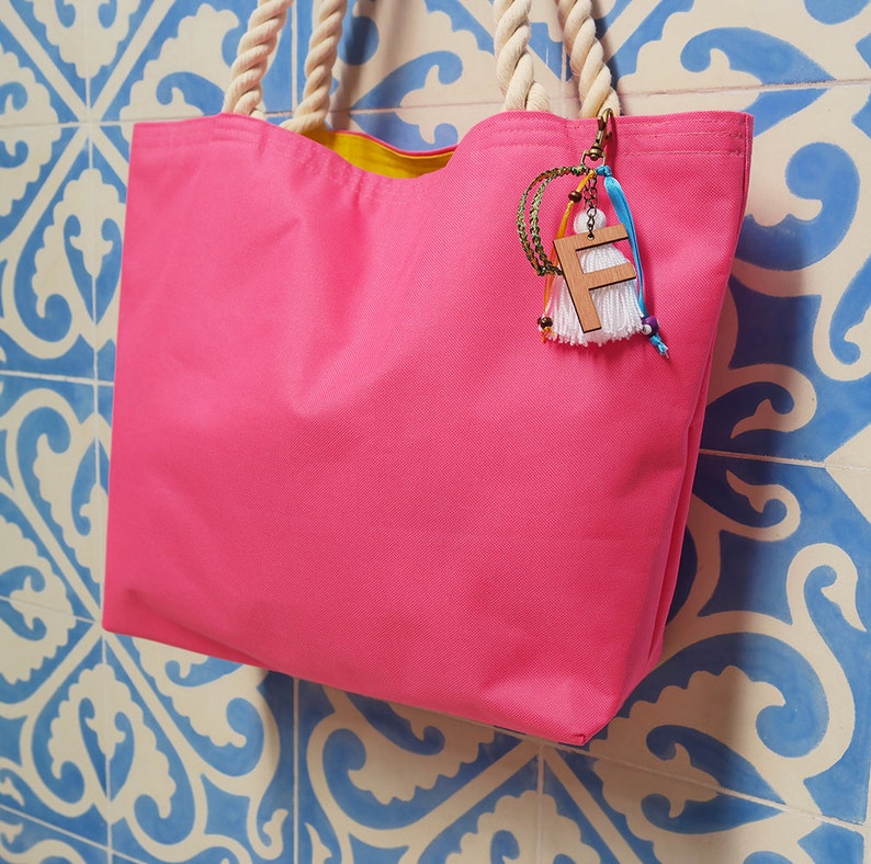 May include: A bright pink tote bag with a yellow lining and a wooden charm with the letter "F" hanging from the handle.