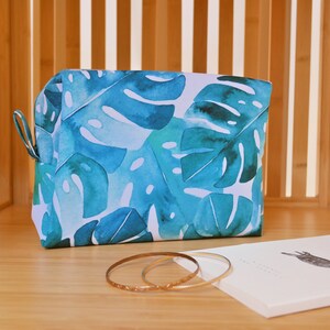 May include: A blue and white toiletry bag with a tropical leaf pattern. The bag is made of fabric and has a zipper closure.