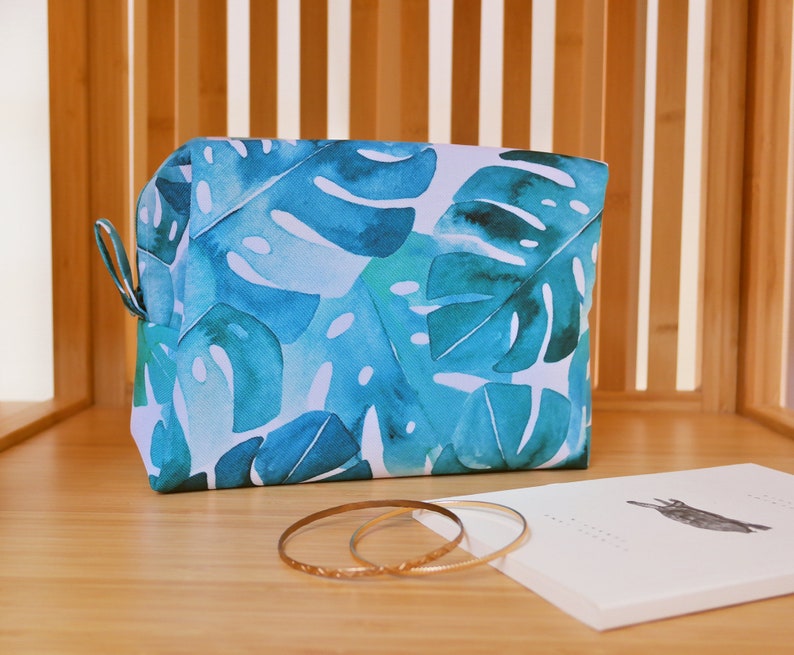 May include: A blue and white toiletry bag with a tropical leaf pattern. The bag is made of fabric and has a zipper closure.