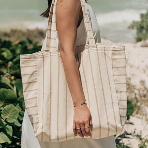 May include: A large, striped tote bag with brown stripes on a cream background. The bag is made of a woven fabric and has a wide, flat base.