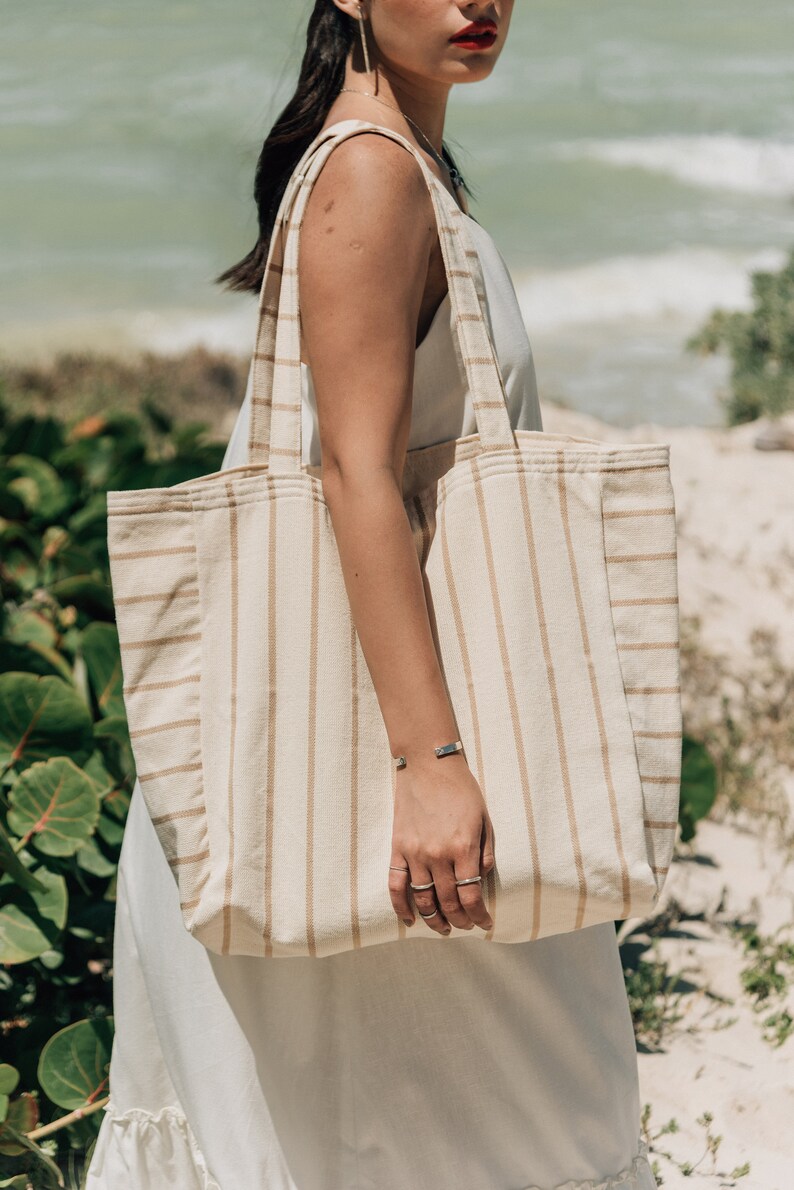 May include: A large, striped tote bag with brown stripes on a cream background. The bag is made of a woven fabric and has a wide, flat base.