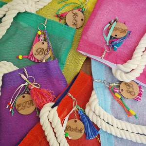 May include: A collection of colourful mesh bags with rope handles and wooden tags. Each tag has a different letter on it, spelling out the word "Beach".