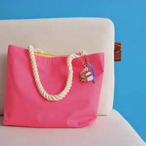 May include: A bright pink tote bag with a white rope handle and a yellow lining. The bag has a colorful charm attached to it.