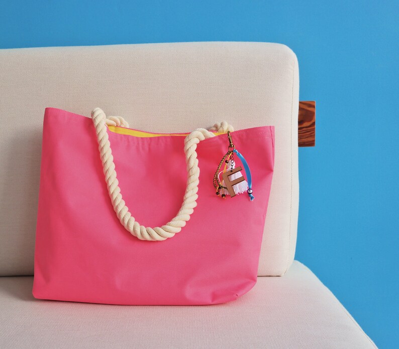 May include: A bright pink tote bag with a white rope handle and a yellow lining. The bag has a colorful charm attached to it.