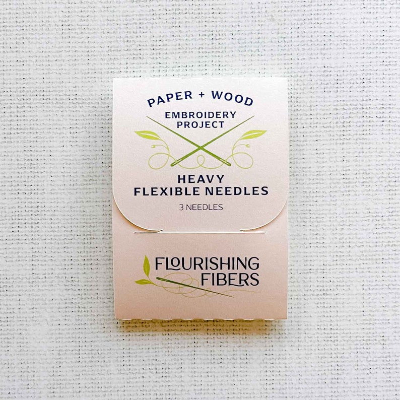May include: A pink and white package of heavy flexible needles for embroidery projects. The package says "Paper + Wood Embroidery Project Heavy Flexible Needles 3 Needles" and "Flourishing Fibers".