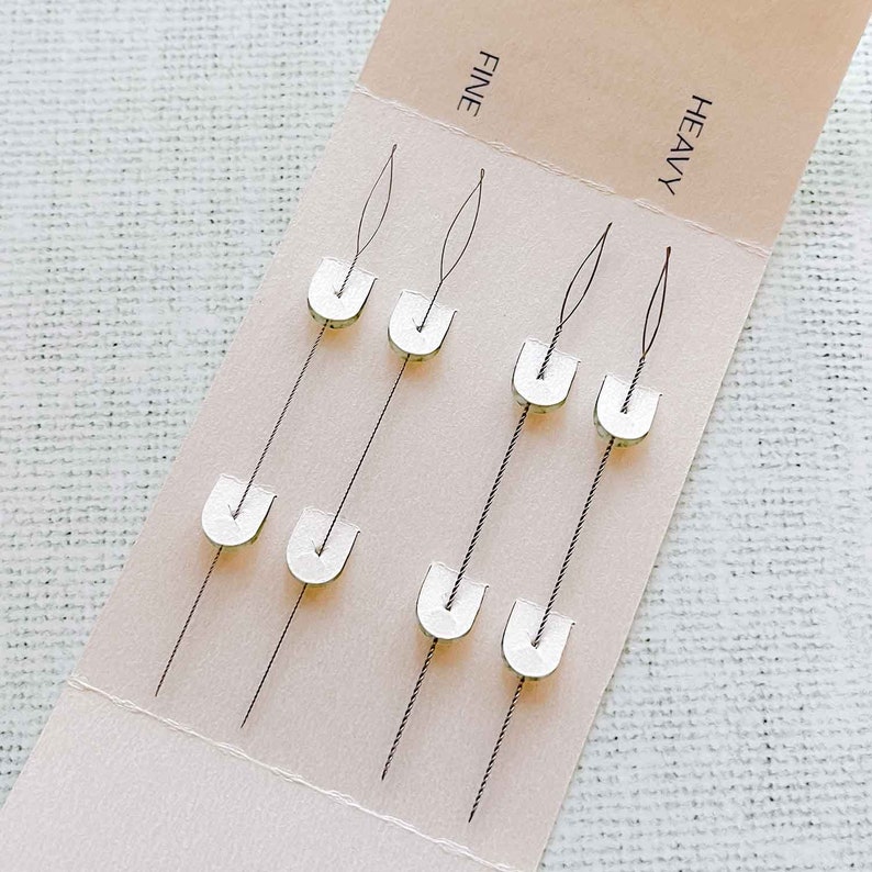 May include: A card with eight needles, labeled "FINE" and "HEAVY", with the needles arranged in two rows of four. The needles have a white plastic tip and are attached to a card.