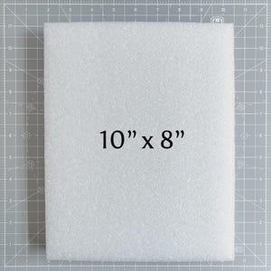 May include: A white foam sheet, measuring 10 inches by 8 inches, is displayed against a gray grid background. The text "10" x 8"" is prominently featured on the foam. The foam has a textured surface.