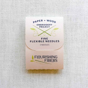 May include: A pink and white package of three fine flexible needles for embroidery. The package is labeled "Paper + Wood Embroidery Project" and "Flourishing Fibers".