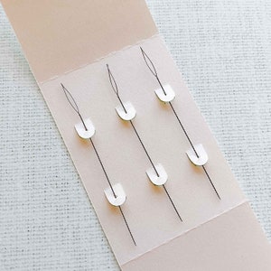 May include: A close-up of a white card with five black threads attached to white plastic loops. The threads are evenly spaced and arranged in a vertical pattern.