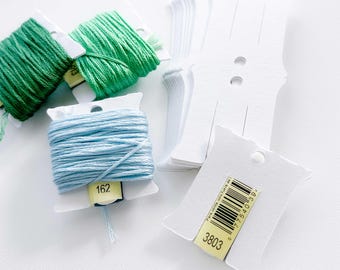 May include: A close-up of two spools of embroidery floss, one light blue and one green, with a white plastic label on each spool. The label on the blue spool has the number 162 printed on it. There are also several white plastic thread organizers with a yellow label that says "3803" and a barcode.