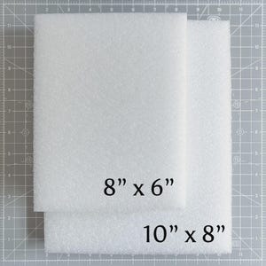 May include: Two white foam sheets, one measuring 8" x 6" and the other 10" x 8", are stacked on a gray cutting mat. The foam has a textured surface. The text "8" x 6"" and "10" x 8"" is printed on the foam.