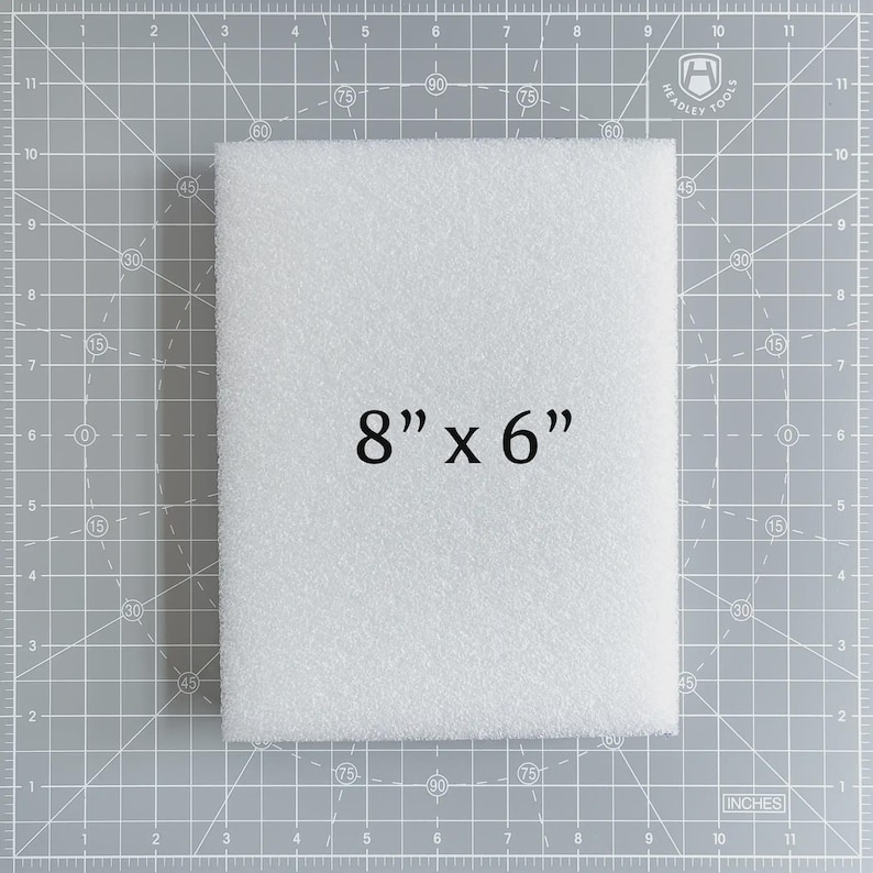 May include: A white, rectangular foam block, measuring 8 inches by 6 inches, is displayed on a gray cutting mat. The text "8" x 6"" is printed in black on the foam. The mat has grid lines and inch measurements.