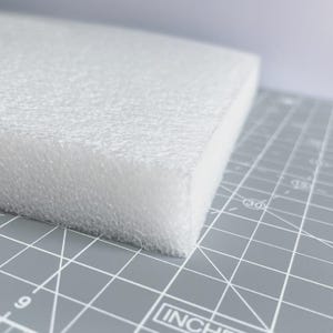 May include: A white foam block with a textured surface. The block is rectangular and sits on a gray cutting mat with inch measurements.