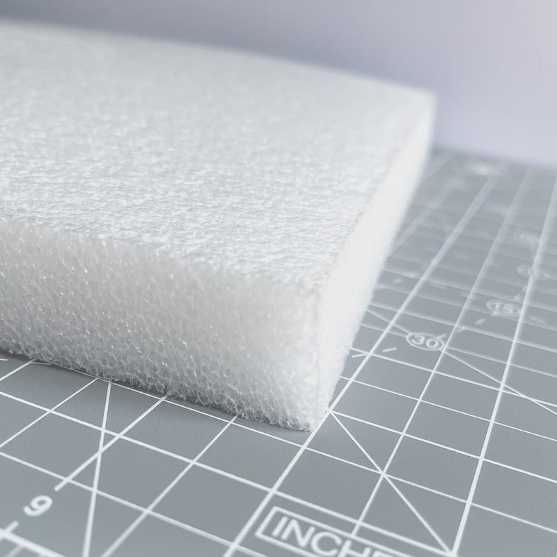 May include: A white foam block with a textured surface. The block is rectangular and sits on a gray cutting mat with inch measurements.