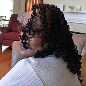 May include: A woman with long, black, curly hair wearing glasses and a light blue shirt.
