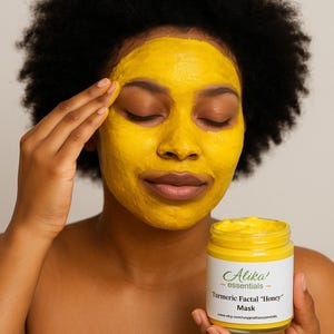 May include: A person applies a yellow turmeric facial mask. The jar of mask is labeled "Alika' essentials - Turmeric Facial "Honey" Mask" and includes the website address www.etsy.com/unyprallionessentials.