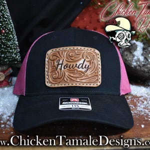 May include: Black and pink trucker hat with a leather patch that says "Howdy". The patch has a decorative border. The hat is a Richardson 115. The hat has a black front and a pink mesh back.
