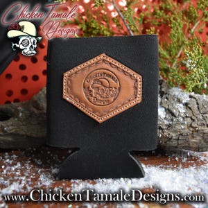 Könnte beinhalten: Schwarzer Getränkehalter mit einem braunen Lederaufnäher mit einem Totenkopf mit Hut und dem Text "Chicken Tamale Designs". Der Halter hat einen sechseckigen Aufnäher mit einer genähten Bordüre. Die Website www.ChickenTamaleDesigns.com befindet sich unten.