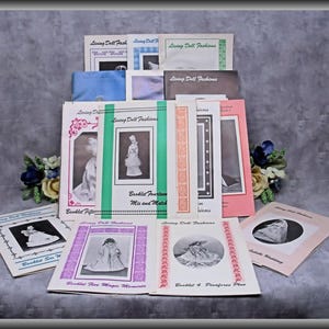 May include: A collection of Living Doll Fashions booklets featuring various designs, including Booklet Fourteen Mix and Match, Booklet Fifteen, Booklet Five Magic Moments, and Booklet 4 Pinafores Plus, with black and white doll photography.