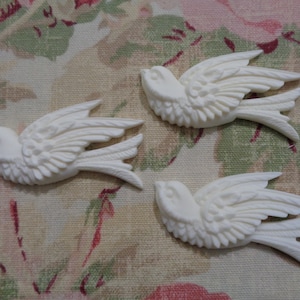 May include: Three white ceramic bird figurines with detailed wings and a textured surface. The birds are arranged in a flying formation.