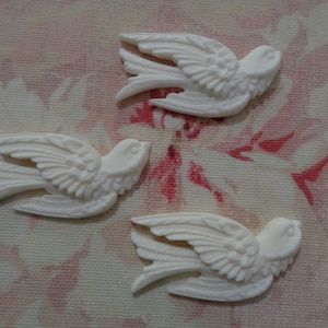 May include: Three white ceramic bird figurines with detailed wings and feathers. The birds are in a flying pose and have a delicate, vintage aesthetic.