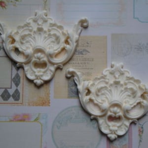 May include: Two white, ornate, decorative wall accents with a floral design. The accents are made of a lightweight material and have a raised, three-dimensional design.