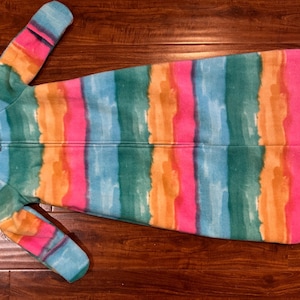 May include: A colorful baby sleep sack with a watercolor stripe design in shades of blue, green, orange, and pink. The sleep sack has a zipper closure and long sleeves. The sleep sack is made of a soft, plush material.