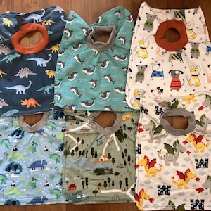 May include: Set of six baby bibs with different patterns. The bibs are made of a soft, absorbent material and feature a variety of colors and designs, including dinosaurs, dolphins, and castles.