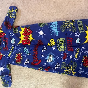 May include: Blue fleece sleep sack with a comic book theme. The sleep sack features a zipper closure and is covered in colorful speech bubbles, stars, and action words like "BAM" and "POW".