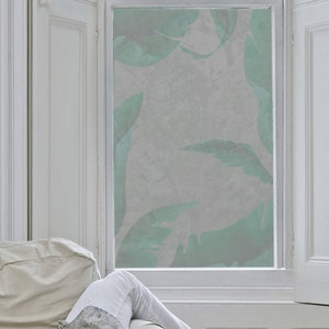 May include: A frosted window film with a leafy pattern in shades of green and gray. The film is applied to a window in a room with white trim and a white couch.