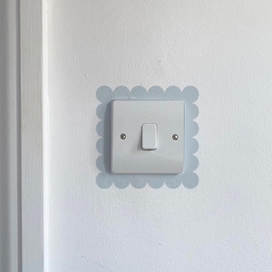 May include: A white light switch with a rectangular plate and a single toggle. The switch is set within a pale blue scalloped border on a white wall. Small screws are visible on the plate.