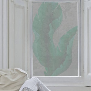 May include: A window with a frosted glass pane featuring a large, abstract, green leaf design. The window is framed in white and is set in a white wall.