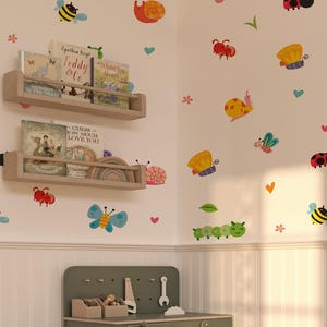 Può includere: Una cameretta per bambini con adesivi murali fantasiosi di insetti, farfalle e fiori. Scaffali in legno contengono libri come "Teddy & Co." e "Guess How Much I Love You". Sotto c'è un banco da lavoro verde con attrezzi giocattolo.