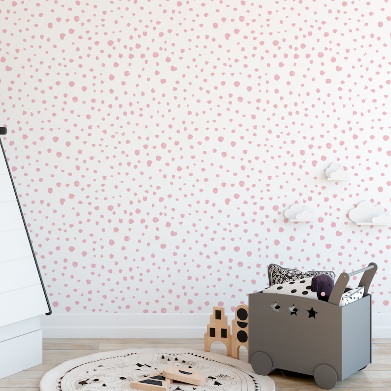 May include: A white wall with a pink polka dot pattern. The wall is in a room with a gray toy storage bin and a round rug with a black and white pattern.