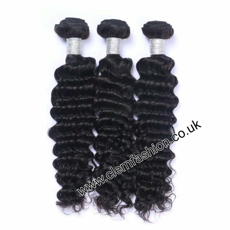 Puede incluir: Tres paquetes de extensiones de cabello humano negro en textura de onda profunda. El cabello est&aacute; atado con una banda plateada en la parte superior.