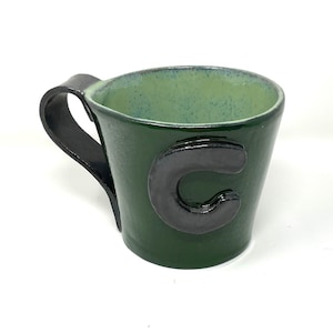 May include: A green ceramic mug with a black handle and a black letter "C" on the front.