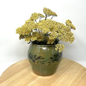 May include: A green ceramic vase with a floral design, filled with dried yellow flowers.