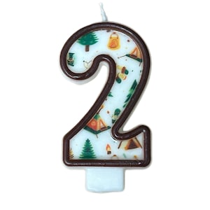 May include: A brown number two candle with a white background featuring a camping theme. The candle has a white wick and is perfect for a birthday cake.