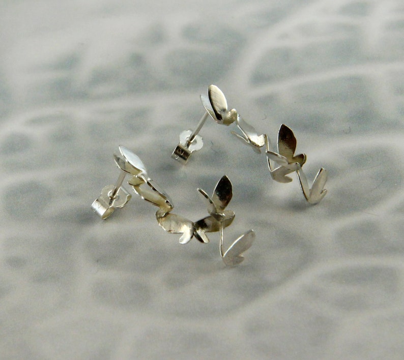 May include: A pair of silver earrings with a leaf design. Each earring has three leaves connected together.