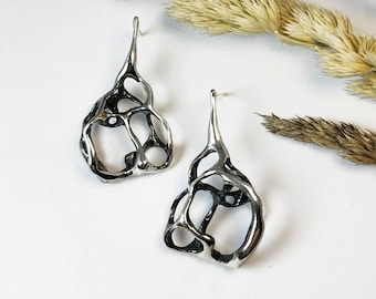 May include: A pair of silver earrings with a unique, organic, and abstract design. The earrings are made of a delicate, openwork metal that resembles a web or a honeycomb.