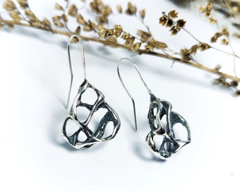 May include: A pair of silver dangle earrings with a unique, openwork design. The earrings are made of a textured metal and have a delicate, organic shape.