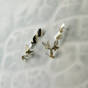 May include: A pair of silver earrings with a design of multiple butterflies connected together.