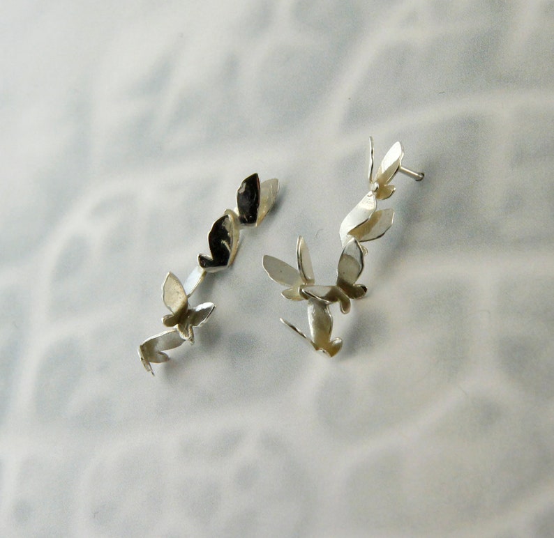 May include: A pair of silver earrings with a design of multiple butterflies connected together.