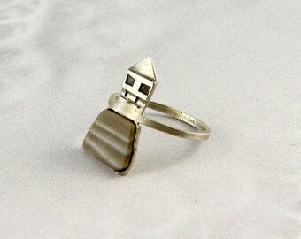 May include: A silver ring with a geometric design and a gray stone set in the center.