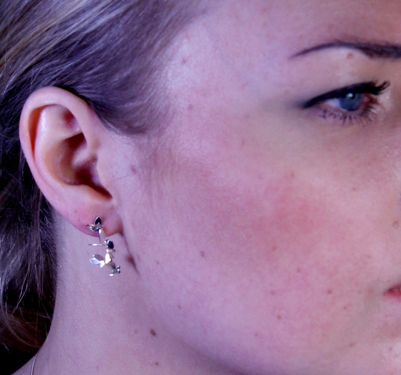 May include: Silver earrings with a delicate leaf design. The earrings are small and dainty, and they would be a great addition to any jewelry collection.
